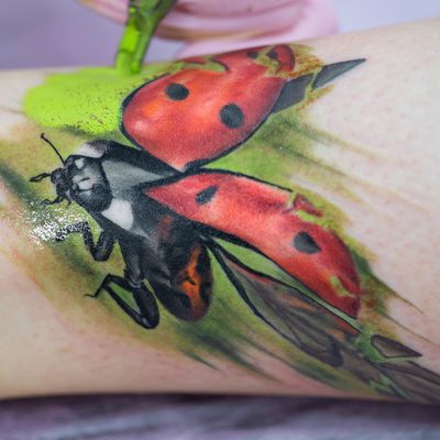 Close-up of a female artist making a color tattoo on the leg of a young girl. Tattoo artist stuffs a ladybug on a girl's leg, tattoo for a girl