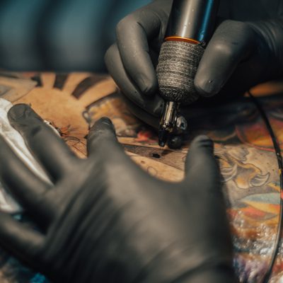 Close up of the tattoo machine. Tattooing. Man creating a picture on his back by a professional tattoo artist.