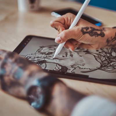 Closeup photo shoot of sketching on digital notepad by girl with tattoed hands.